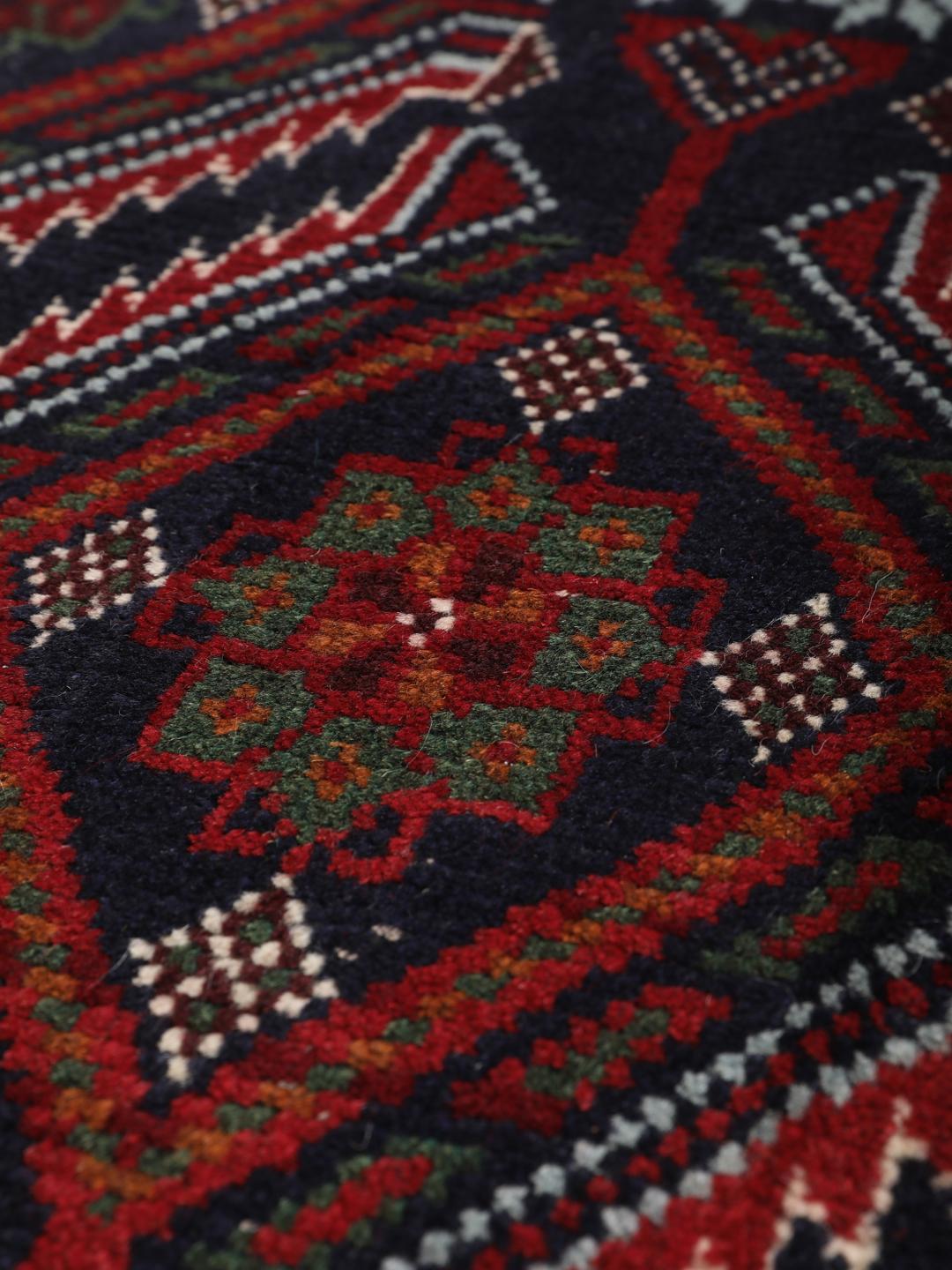 A hand-knotted Baluch rug from the Middle East featuring a dark-red and black geometric pattern.
