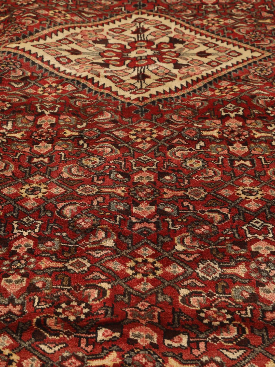 Een handgeknoopt donkerrood Hosseinabad-tapijt met ingewikkelde geometrische patronen.