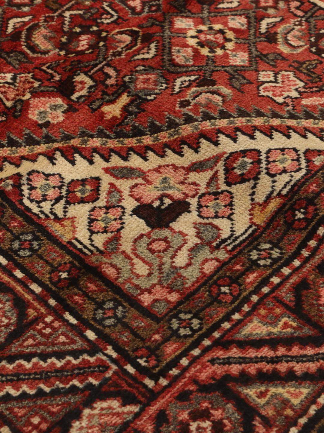 Een handgeknoopt donkerrood Hosseinabad-tapijt met ingewikkelde geometrische patronen.