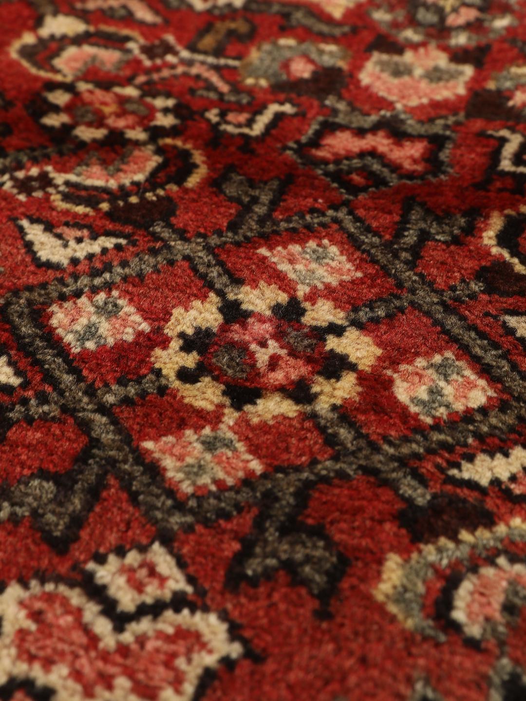 Een handgeknoopt donkerrood Hosseinabad-tapijt met ingewikkelde geometrische patronen.