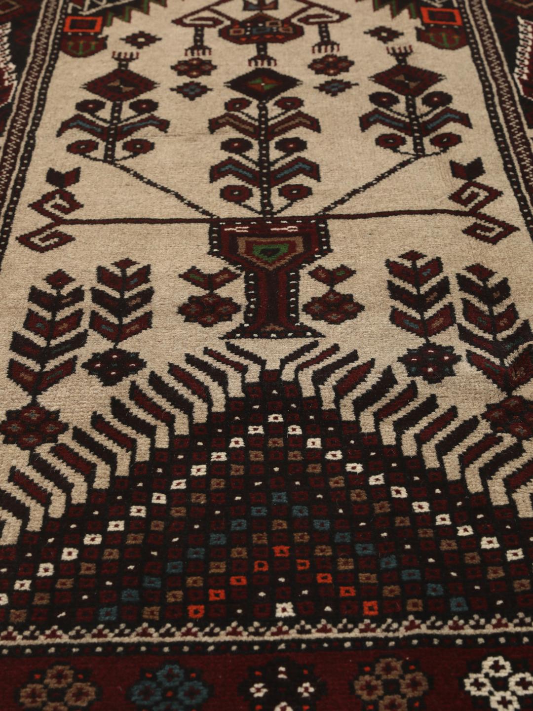 Et håndknyttet Baluch-tæppe fra Mellemøsten med et mørkerødt og beige tribal-design