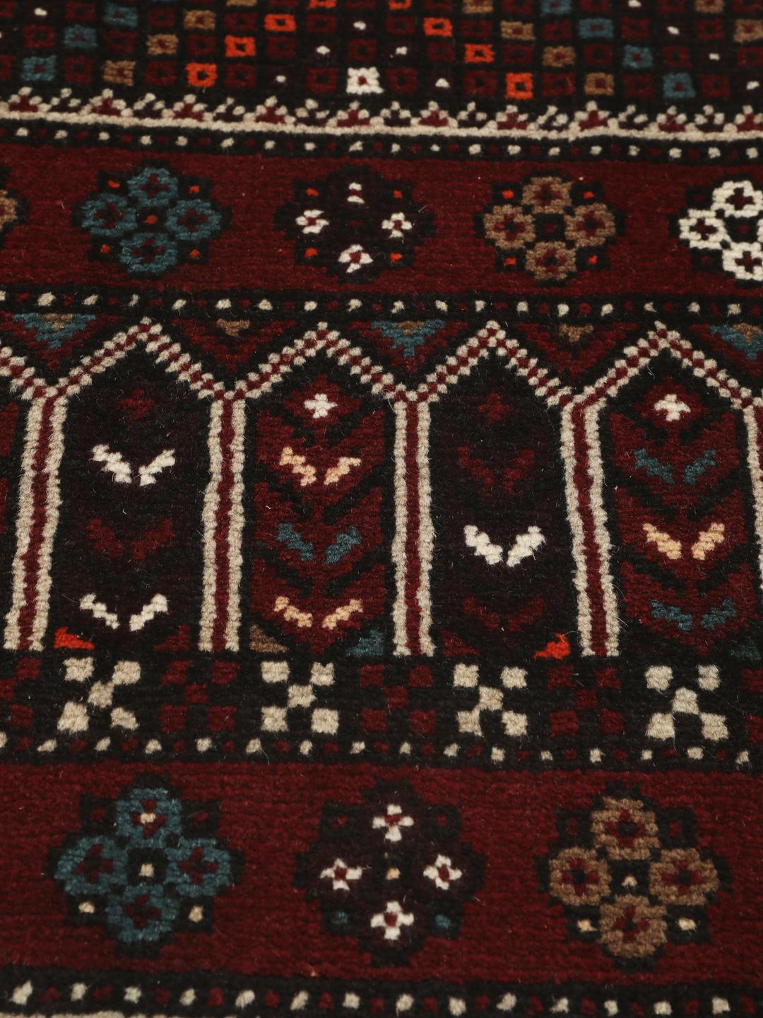Et håndknyttet Baluch-tæppe fra Mellemøsten med et mørkerødt og beige tribal-design