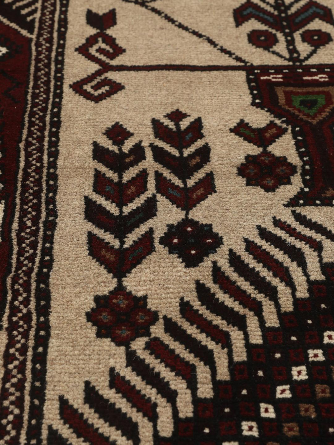 Et håndknyttet Baluch-tæppe fra Mellemøsten med et mørkerødt og beige tribal-design