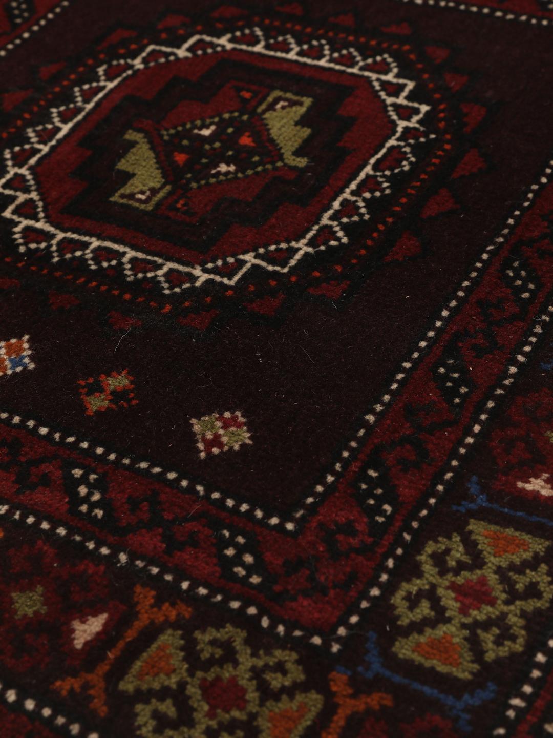 Et håndknyttet Beluch-tæppe fra Mellemøsten i dybe røde nuancer med geometriske motiver.