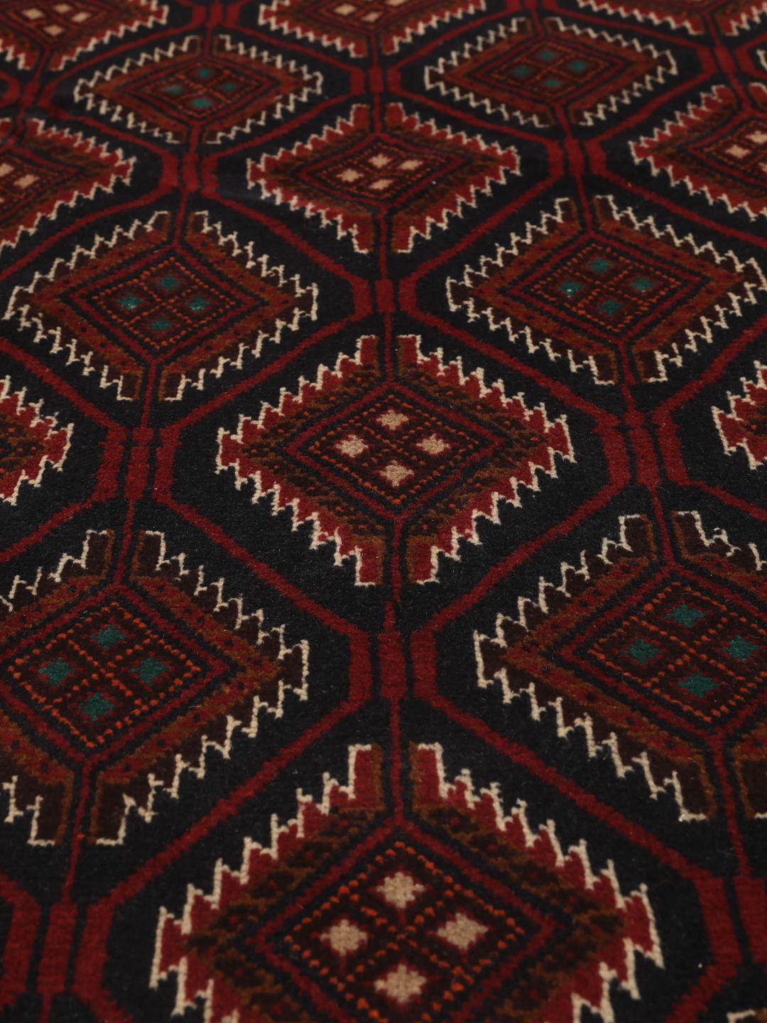 Handgeknoopt Beluch-tapijt uit het Midden-Oosten in donkerrode en donkerblauwe tinten met geometrische motieven.