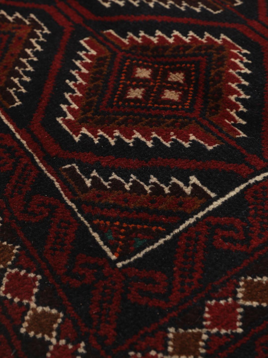 Handgeknoopt Beluch-tapijt uit het Midden-Oosten in donkerrode en donkerblauwe tinten met geometrische motieven.