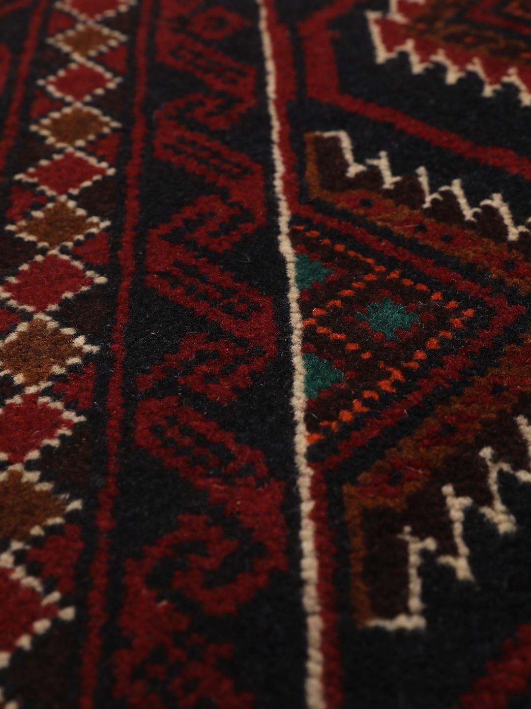 Handgeknoopt Beluch-tapijt uit het Midden-Oosten in donkerrode en donkerblauwe tinten met geometrische motieven.