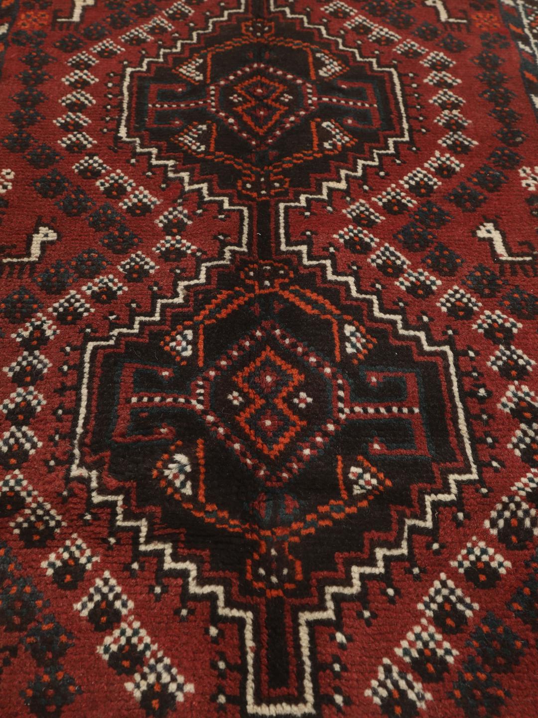 Et håndknyttet Shiraz-tæppe fra Mellemøsten med et mørkerødt og sort geometrisk design.