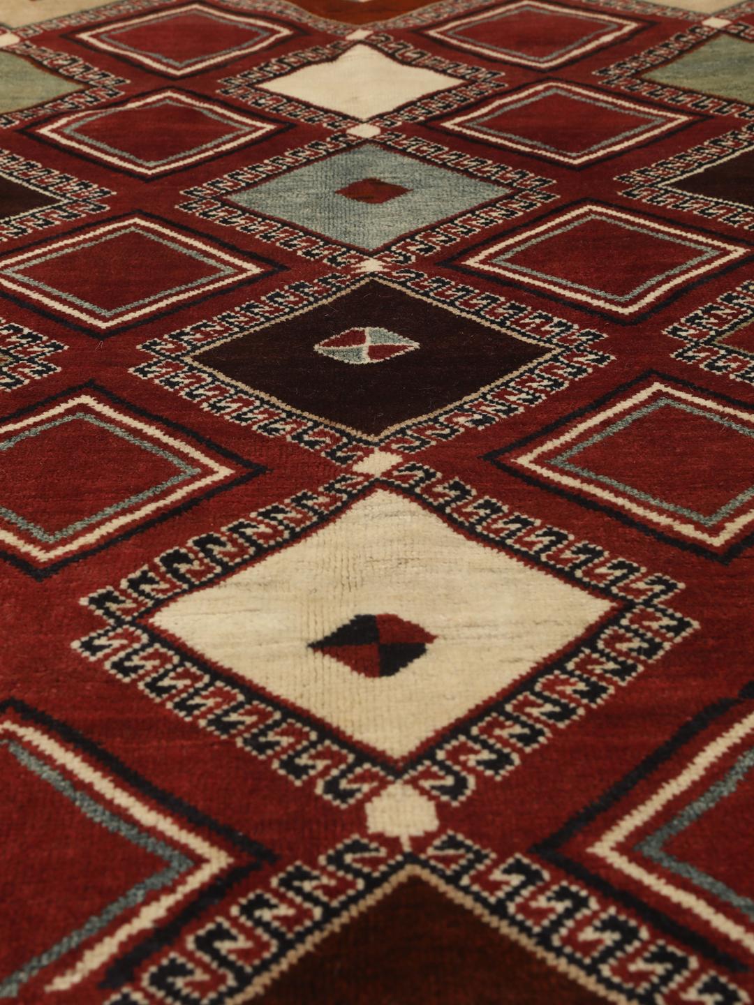 Hand-knotted Ghashghai rug from the Middle East featuring a vibrant red field with geometric diamond motifs.