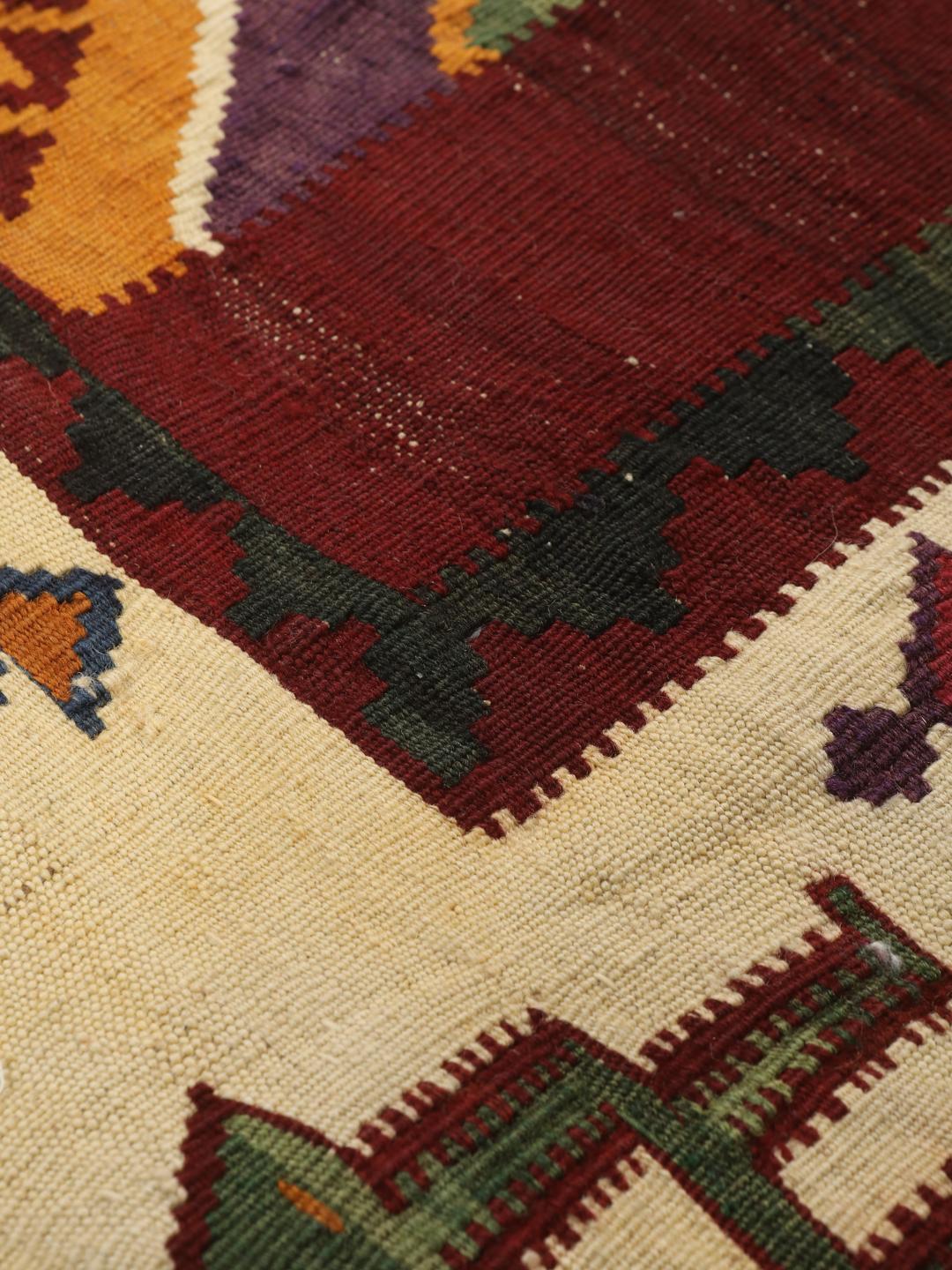 Un tapis kilim vintage tissé à la main provenant du Moyen-Orient, arborant de grands motifs géométriques en forme de losanges dans des tons rouge, vert et crème.