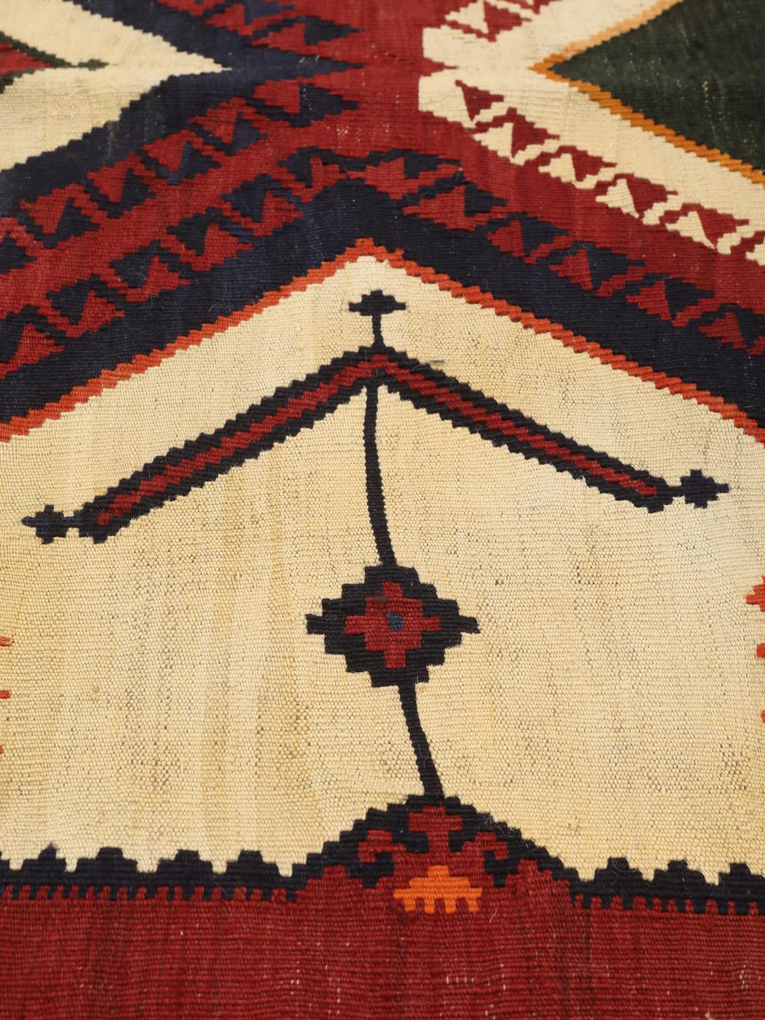 Un tapis kilim vintage tissé à la main provenant du Moyen-Orient, arborant de grands motifs géométriques en forme de losanges dans des tons rouge, vert et crème.
