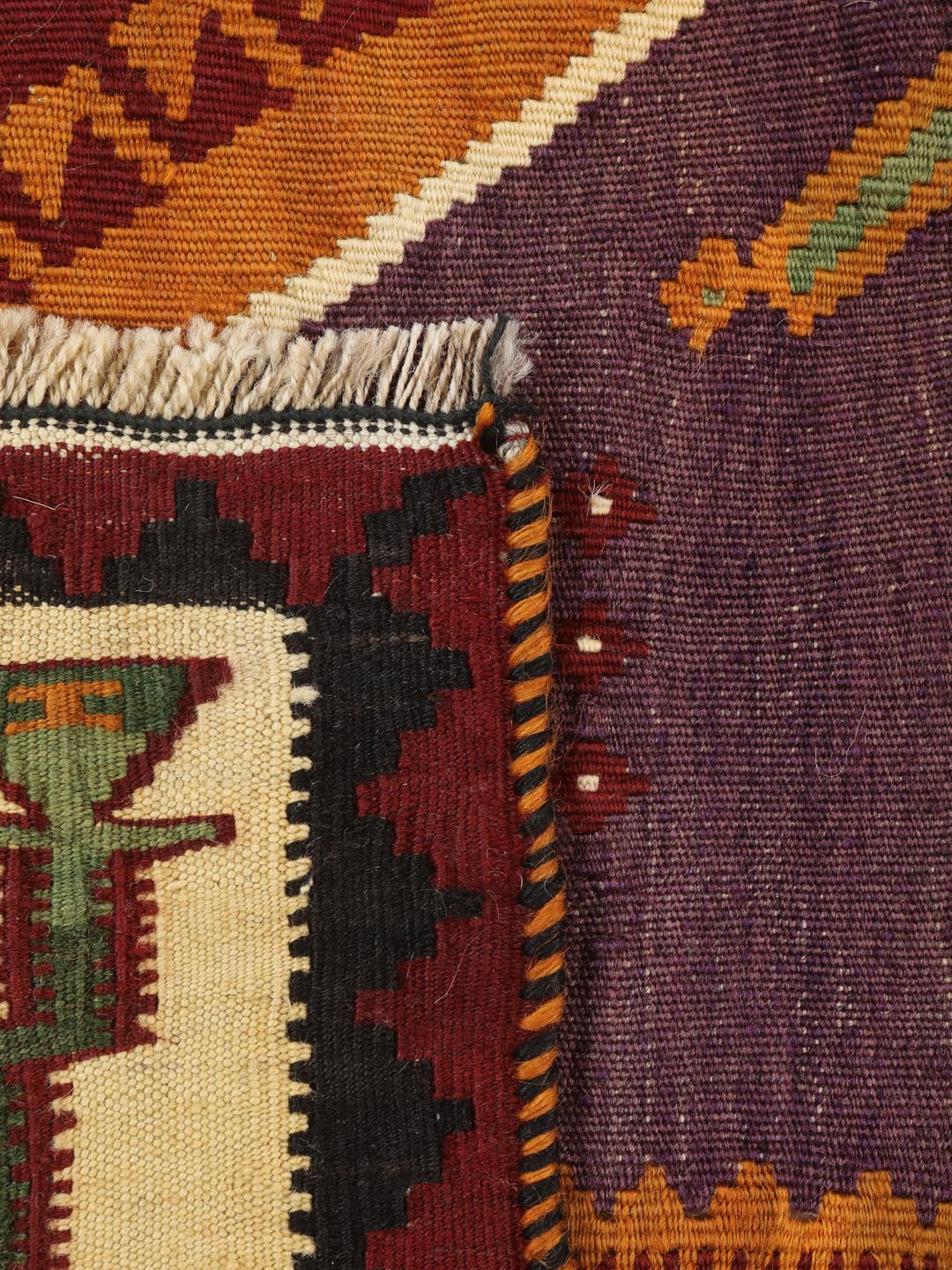 Un tapis kilim vintage tissé à la main provenant du Moyen-Orient, arborant de grands motifs géométriques en forme de losanges dans des tons rouge, vert et crème.