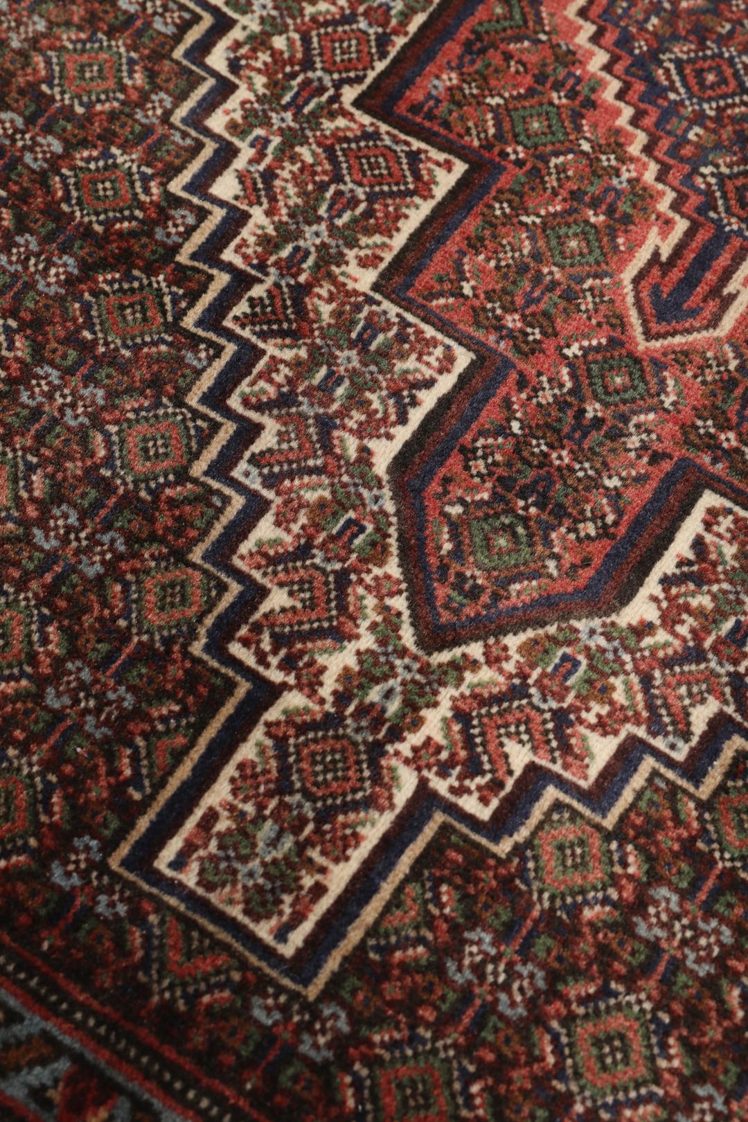 A hand-knotted Senneh rug from the Middle East in dark-red and dark-blue tones.