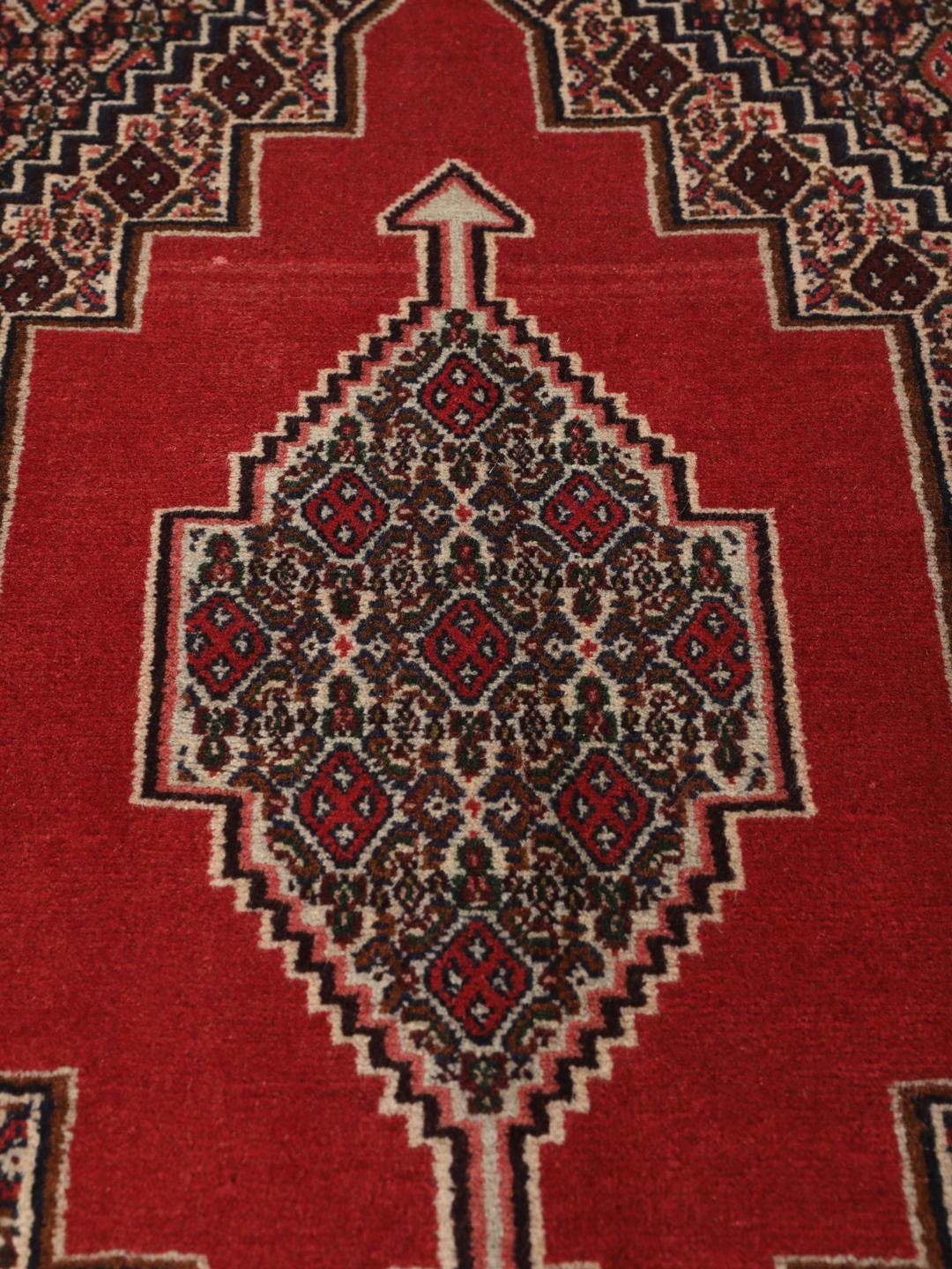 A hand-knotted Senneh rug from the Middle East in red with geometric motifs.