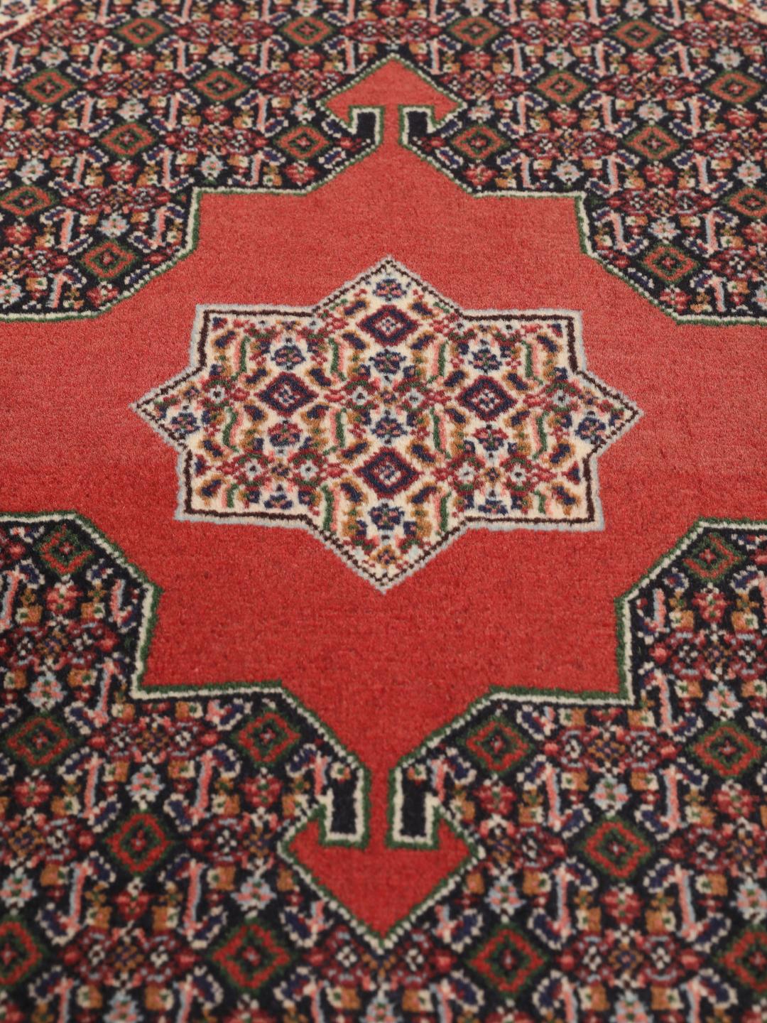 A hand-knotted Senneh rug from the Middle East featuring a red and dark-blue patterned design.