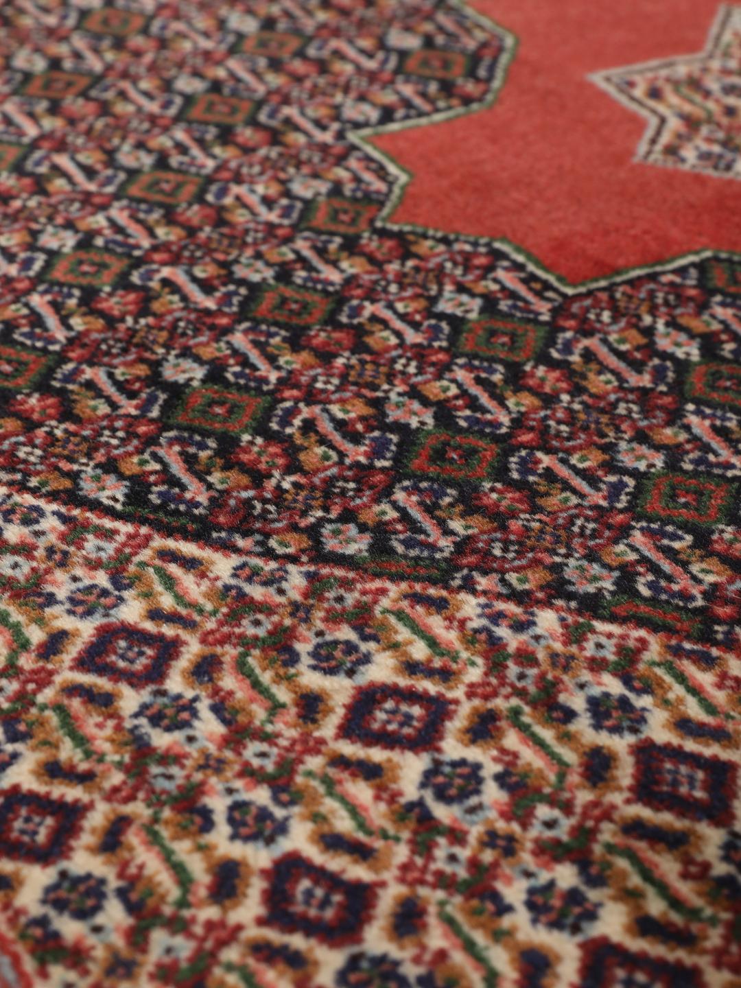 A hand-knotted Senneh rug from the Middle East featuring a red and dark-blue patterned design.