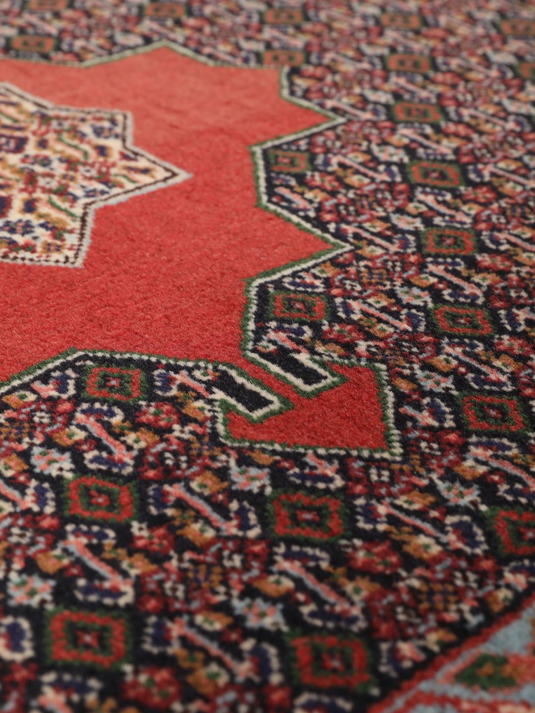 A hand-knotted Senneh rug from the Middle East featuring a red and dark-blue patterned design.