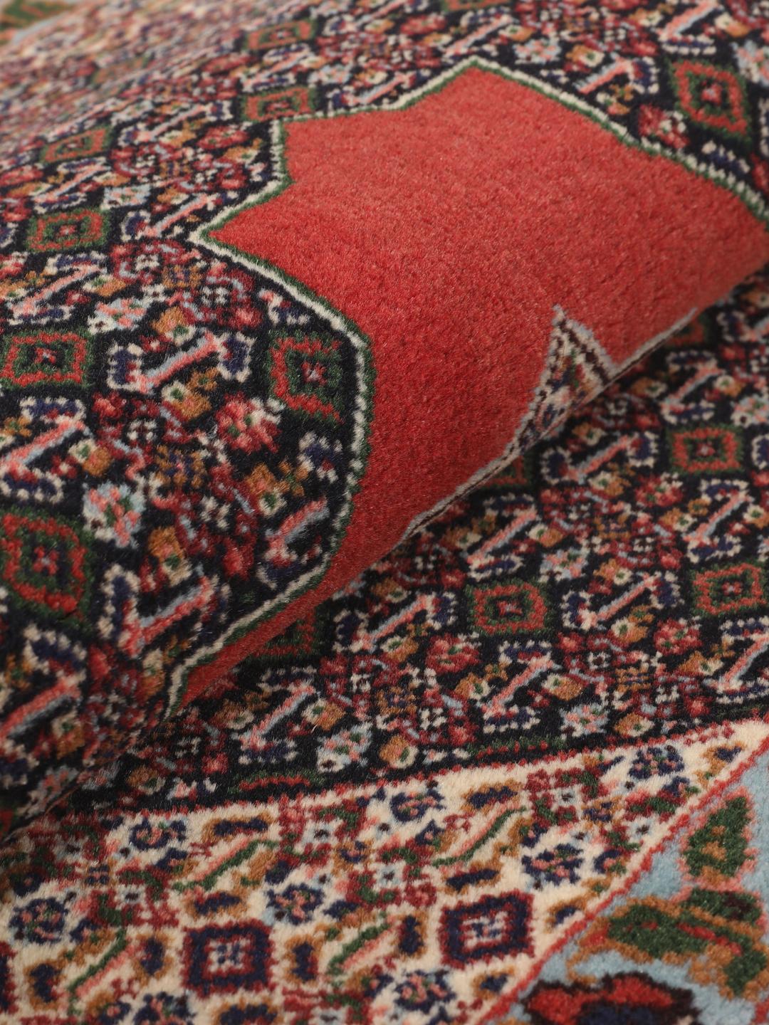 A hand-knotted Senneh rug from the Middle East featuring a red and dark-blue patterned design.