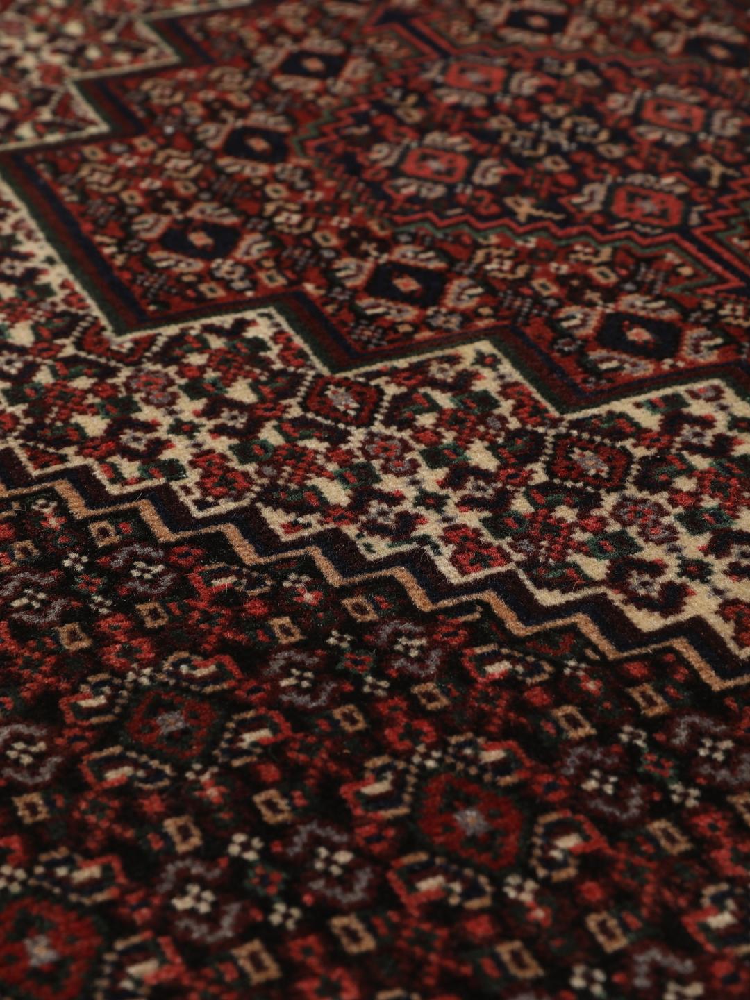Ein handgeknüpfter Senneh-Teppich mit einem dunkelroten und schwarzen geometrischen Muster.