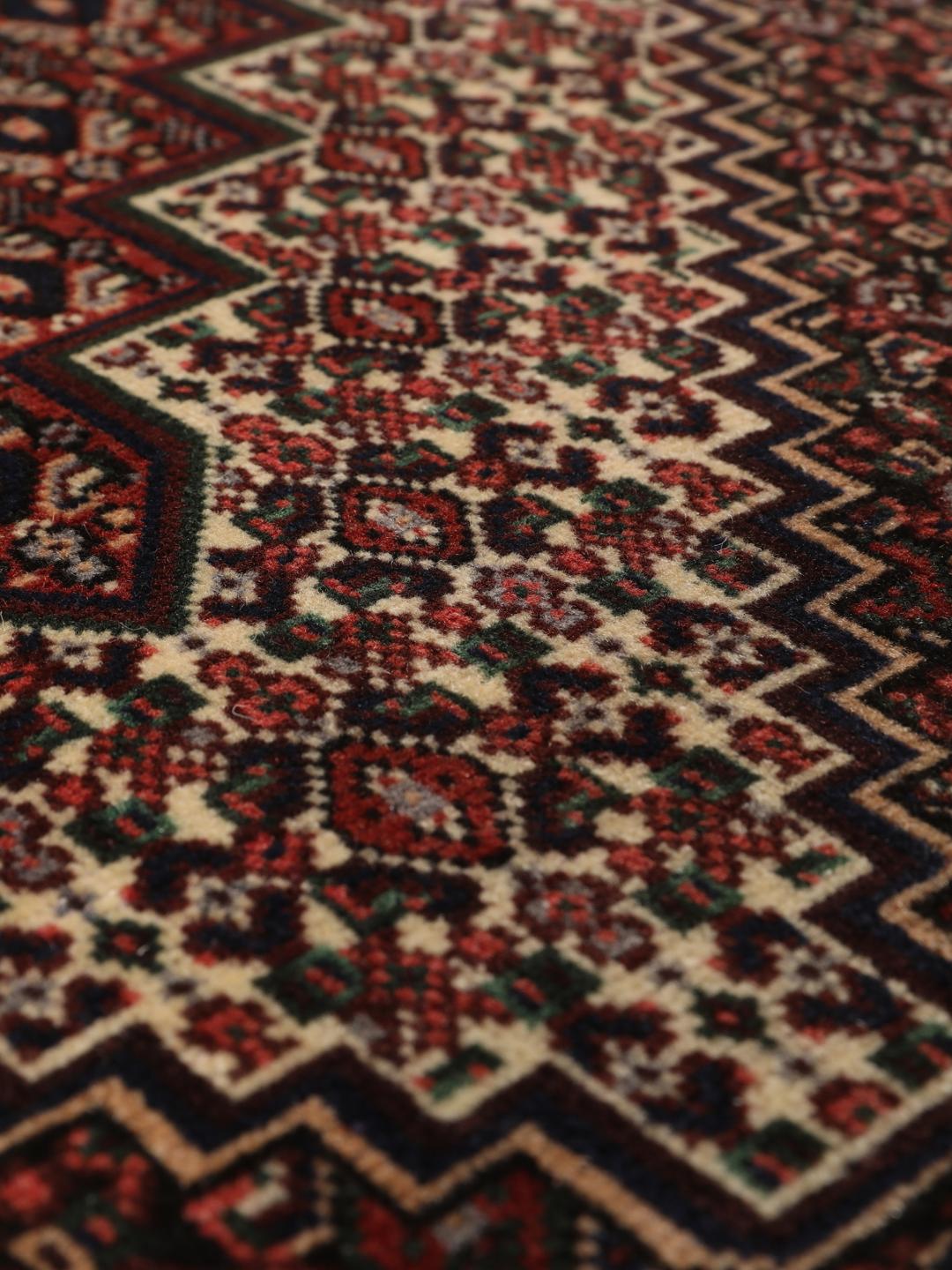 Ein handgeknüpfter Senneh-Teppich mit einem dunkelroten und schwarzen geometrischen Muster.