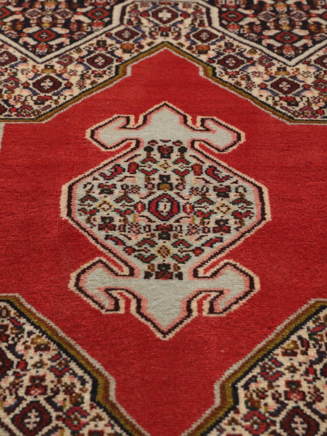 Een handgeknoopt Senneh-tapijt met een levendig rood veld en gedetailleerde bloemmotieven uit het Midden-Oosten.