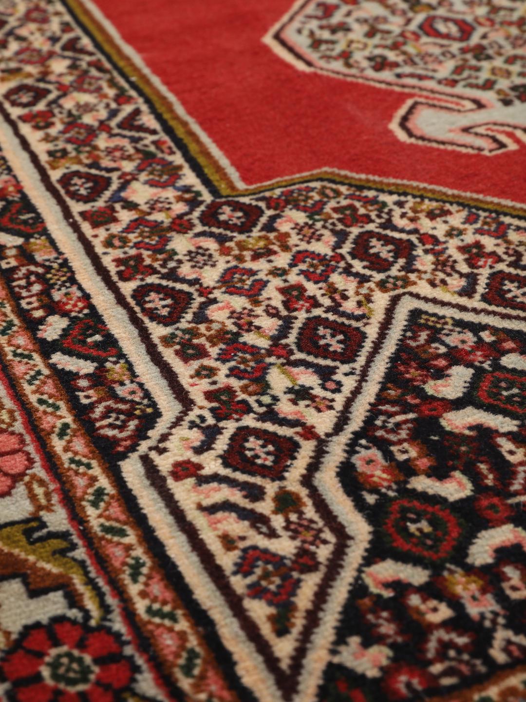 Een handgeknoopt Senneh-tapijt met een levendig rood veld en gedetailleerde bloemmotieven uit het Midden-Oosten.