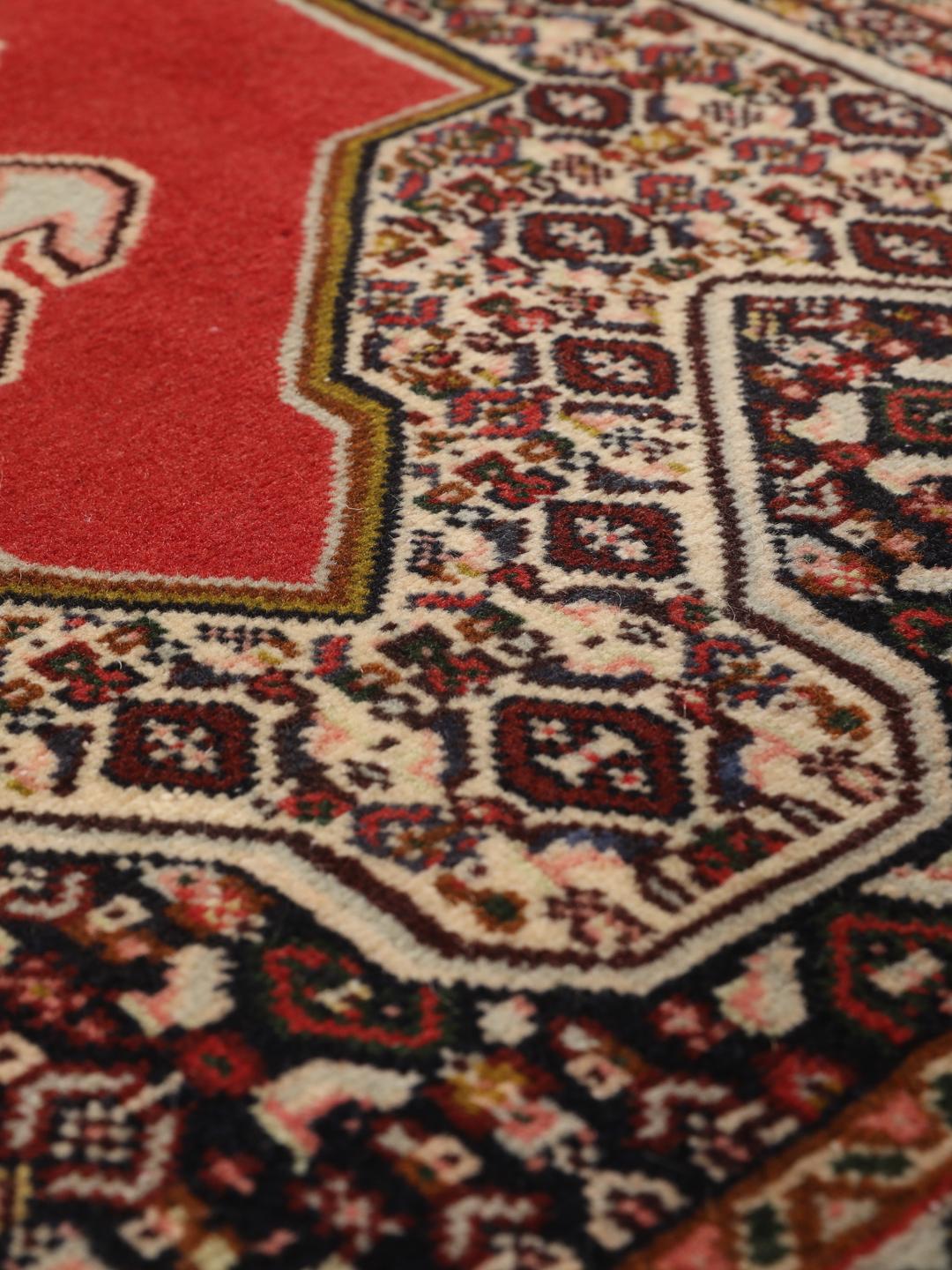 Een handgeknoopt Senneh-tapijt met een levendig rood veld en gedetailleerde bloemmotieven uit het Midden-Oosten.