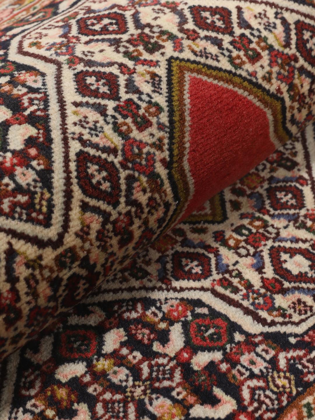 Een handgeknoopt Senneh-tapijt met een levendig rood veld en gedetailleerde bloemmotieven uit het Midden-Oosten.
