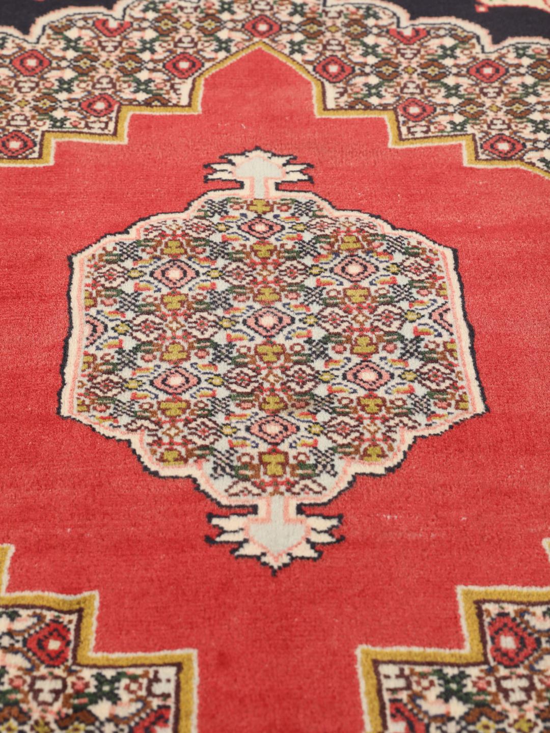 Een handgeknoopt Senneh-tapijt uit het Midden-Oosten met een rood veld en decoratieve bloemenranden.
