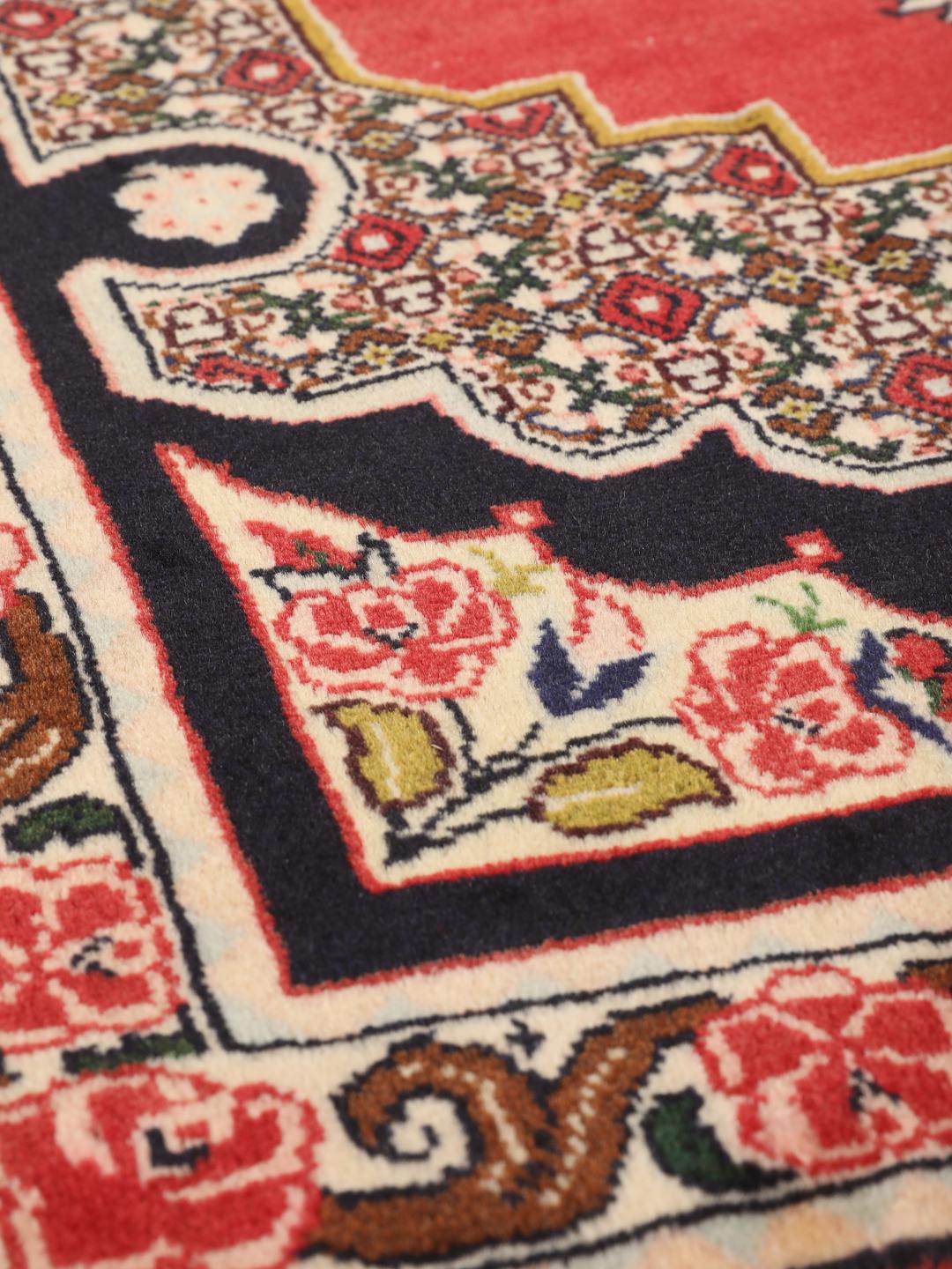 Een handgeknoopt Senneh-tapijt uit het Midden-Oosten met een rood veld en decoratieve bloemenranden.
