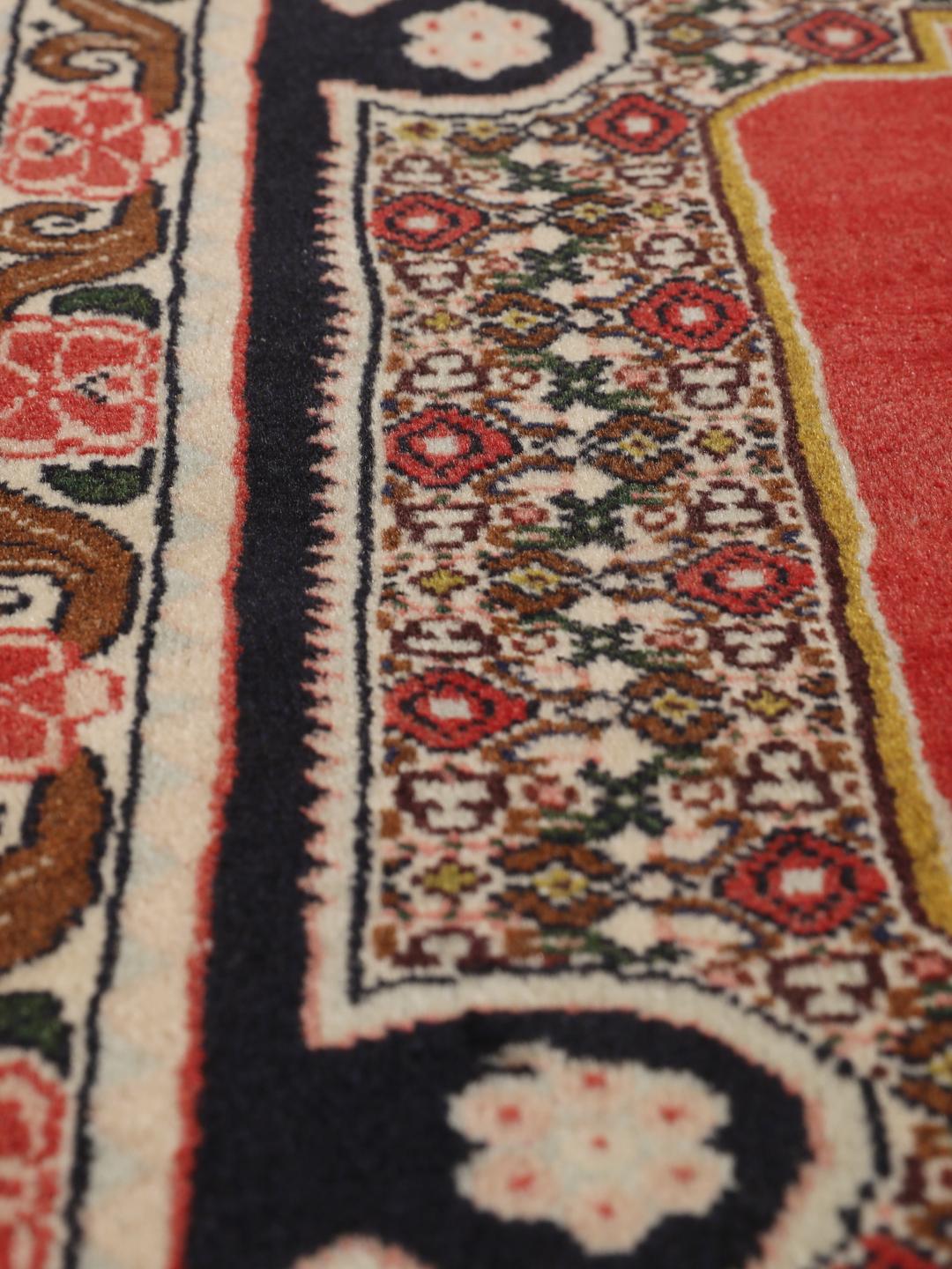 Een handgeknoopt Senneh-tapijt uit het Midden-Oosten met een rood veld en decoratieve bloemenranden.