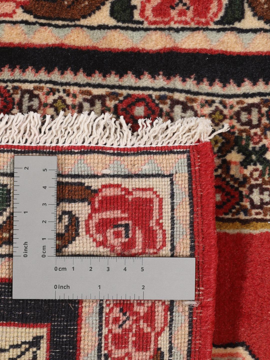 Een handgeknoopt Senneh-tapijt uit het Midden-Oosten met een rood veld en decoratieve bloemenranden.