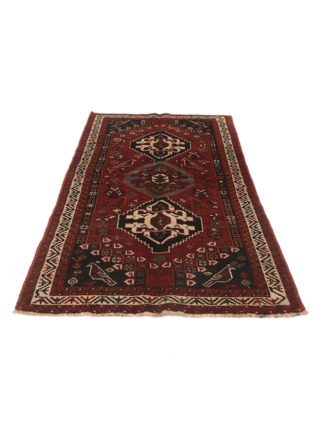 Een handgeknoopt Shiraz-tapijt uit het Midden-Oosten met een donkerrood veld en geometrische motieven.