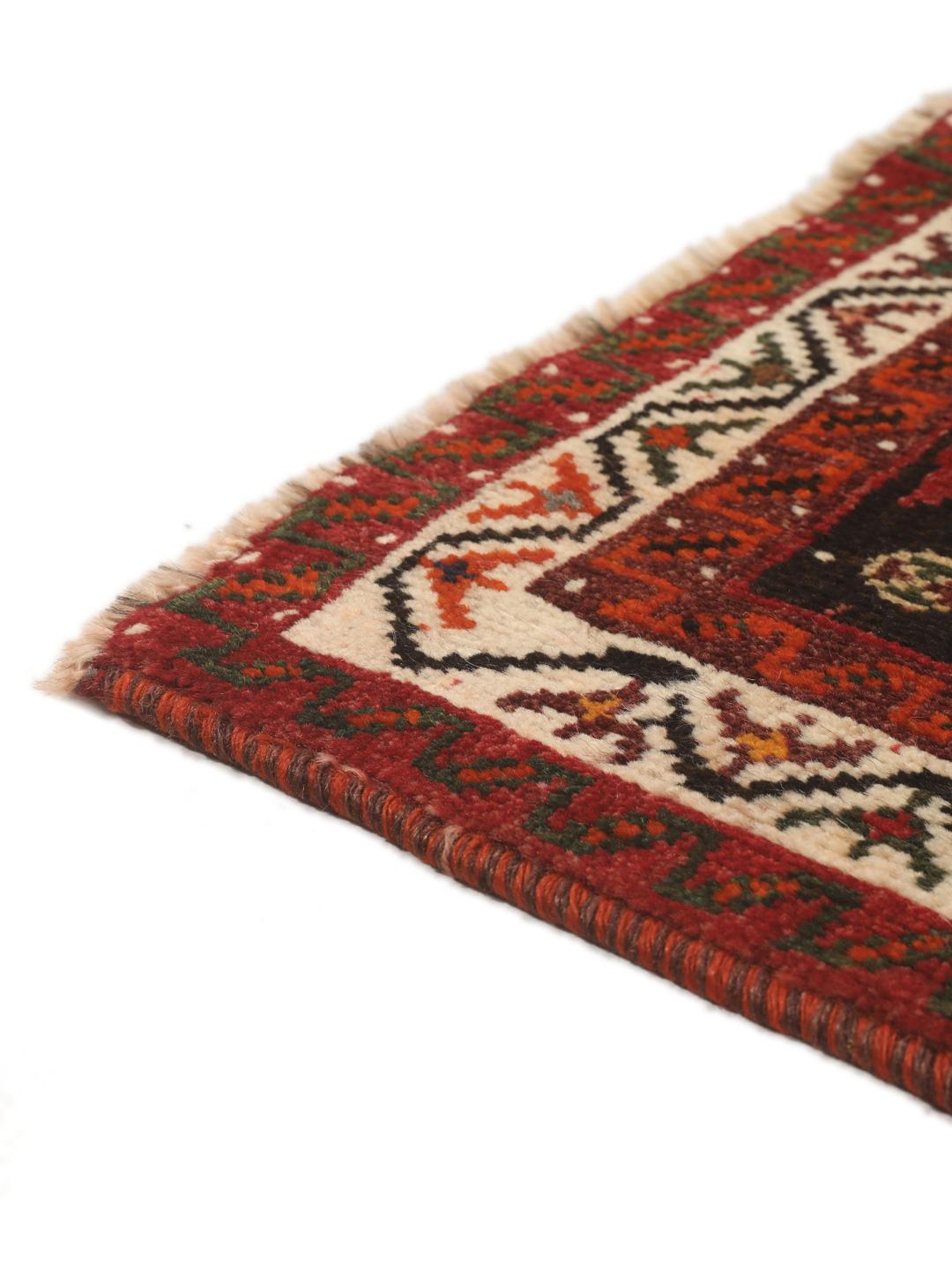 Een handgeknoopt Shiraz-tapijt uit het Midden-Oosten met een donkerrood veld en geometrische motieven.