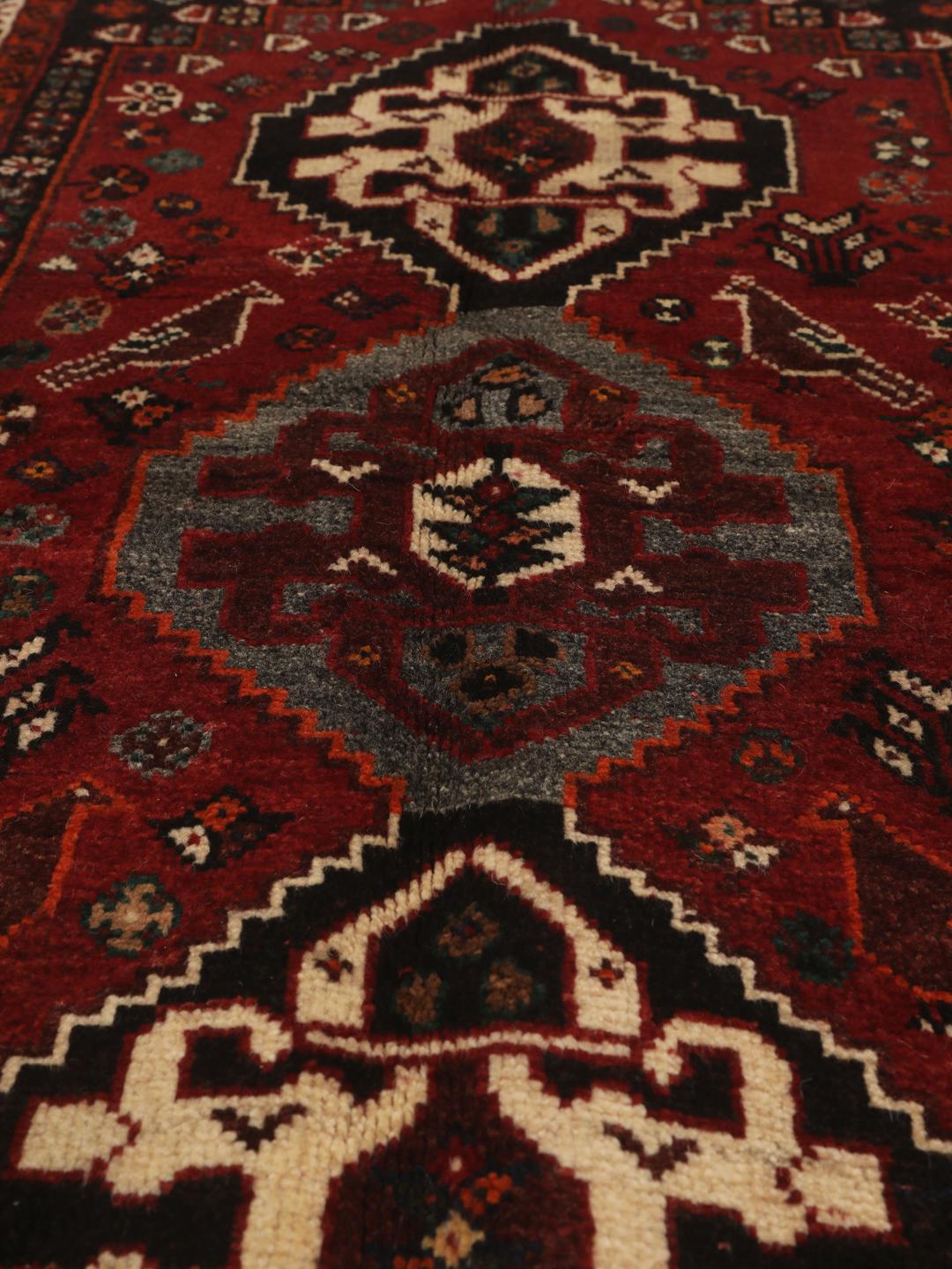 Een handgeknoopt Shiraz-tapijt uit het Midden-Oosten met een donkerrood veld en geometrische motieven.