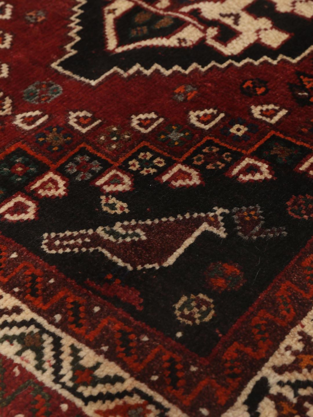 Een handgeknoopt Shiraz-tapijt uit het Midden-Oosten met een donkerrood veld en geometrische motieven.
