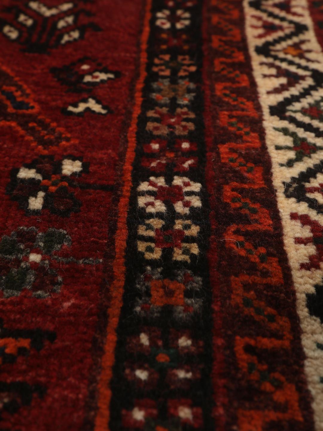 Een handgeknoopt Shiraz-tapijt uit het Midden-Oosten met een donkerrood veld en geometrische motieven.