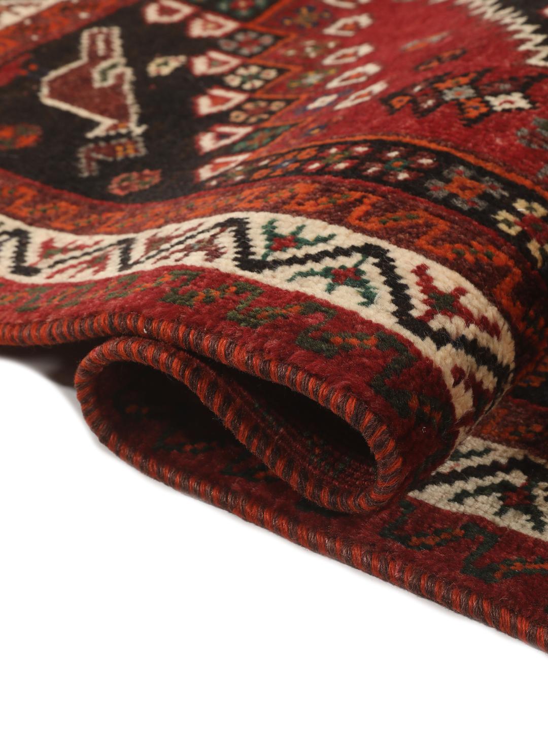 Een handgeknoopt Shiraz-tapijt uit het Midden-Oosten met een donkerrood veld en geometrische motieven.