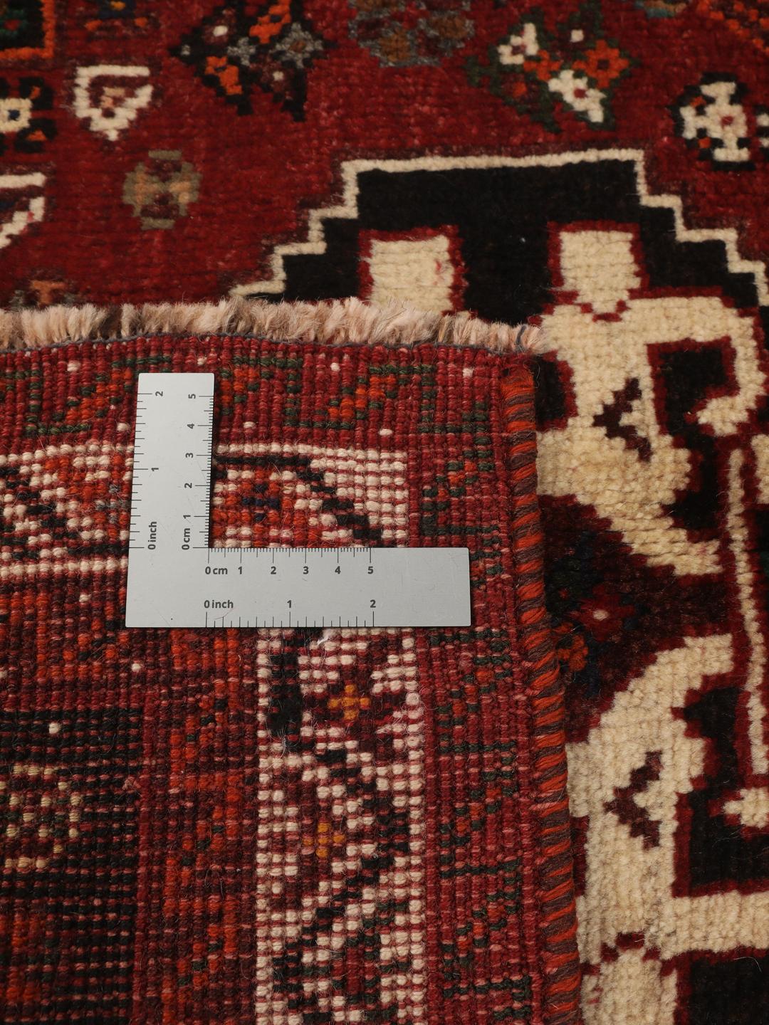 Een handgeknoopt Shiraz-tapijt uit het Midden-Oosten met een donkerrood veld en geometrische motieven.