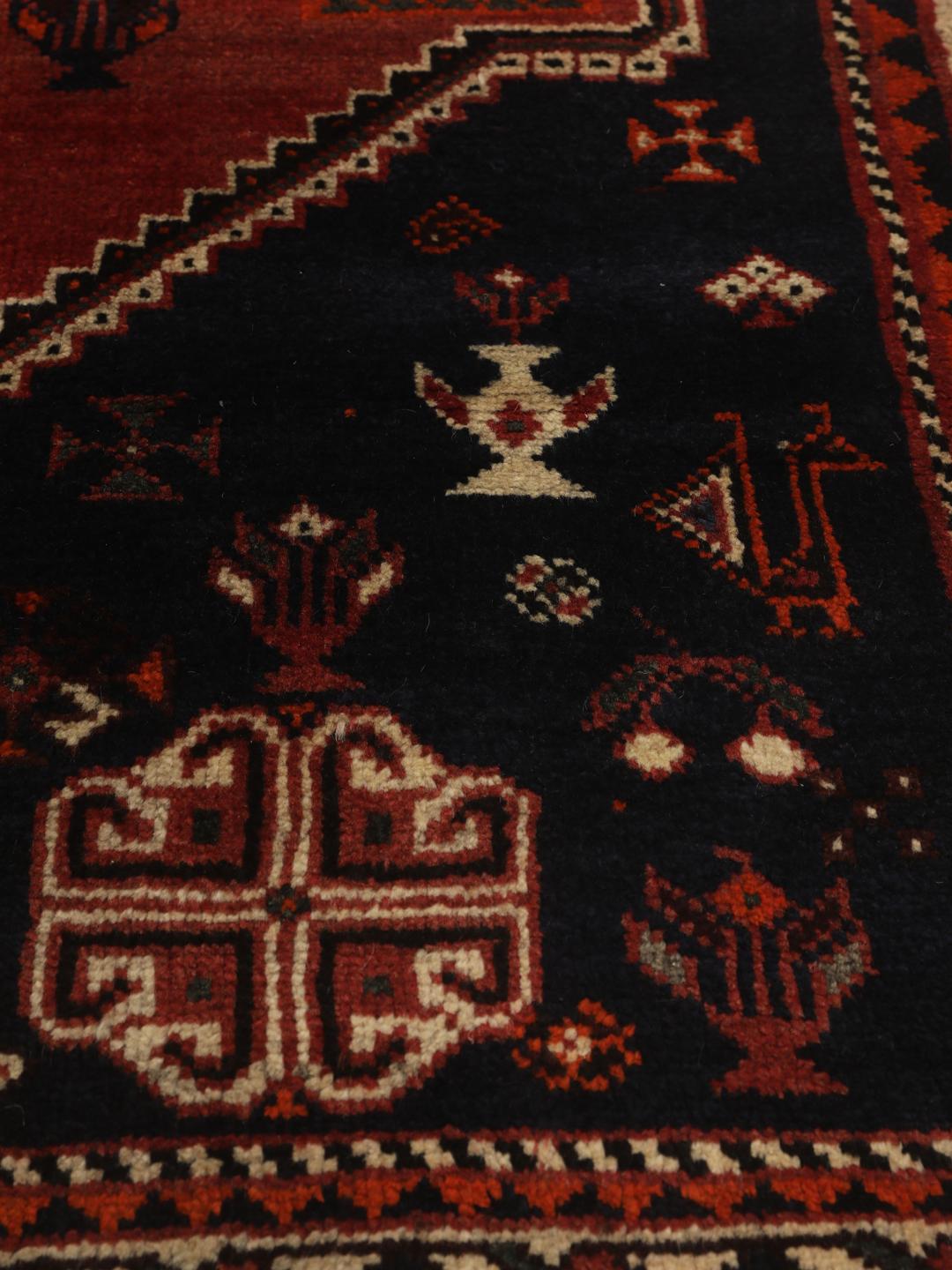 Een rechthoekig handgeknoopt Ghashghai tapijt uit het Midden-Oosten met een donkerrood en donkerblauw palet met geometrische motieven.
