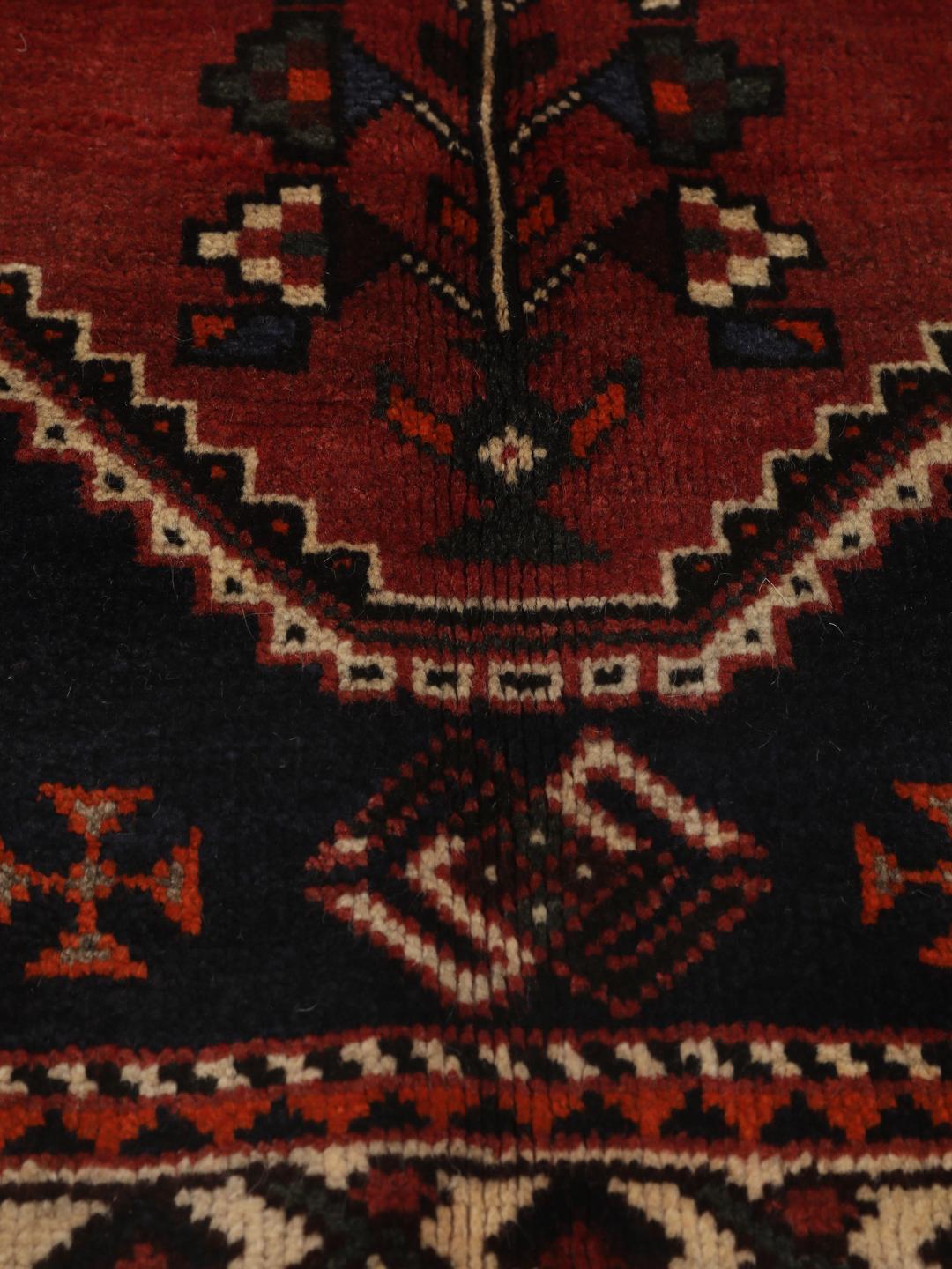 Een rechthoekig handgeknoopt Ghashghai tapijt uit het Midden-Oosten met een donkerrood en donkerblauw palet met geometrische motieven.