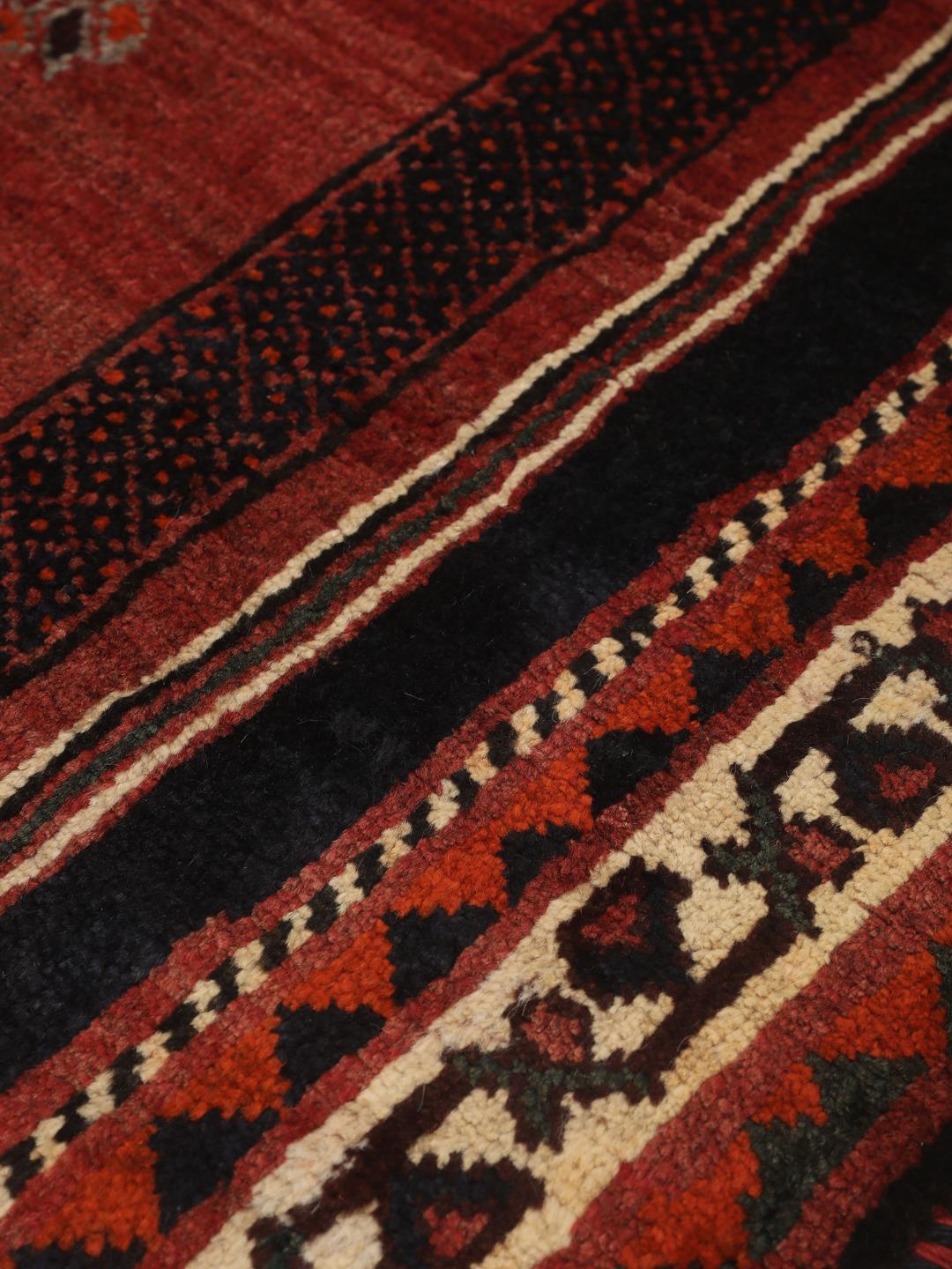 Een rechthoekig handgeknoopt Ghashghai tapijt uit het Midden-Oosten met een donkerrood en donkerblauw palet met geometrische motieven.