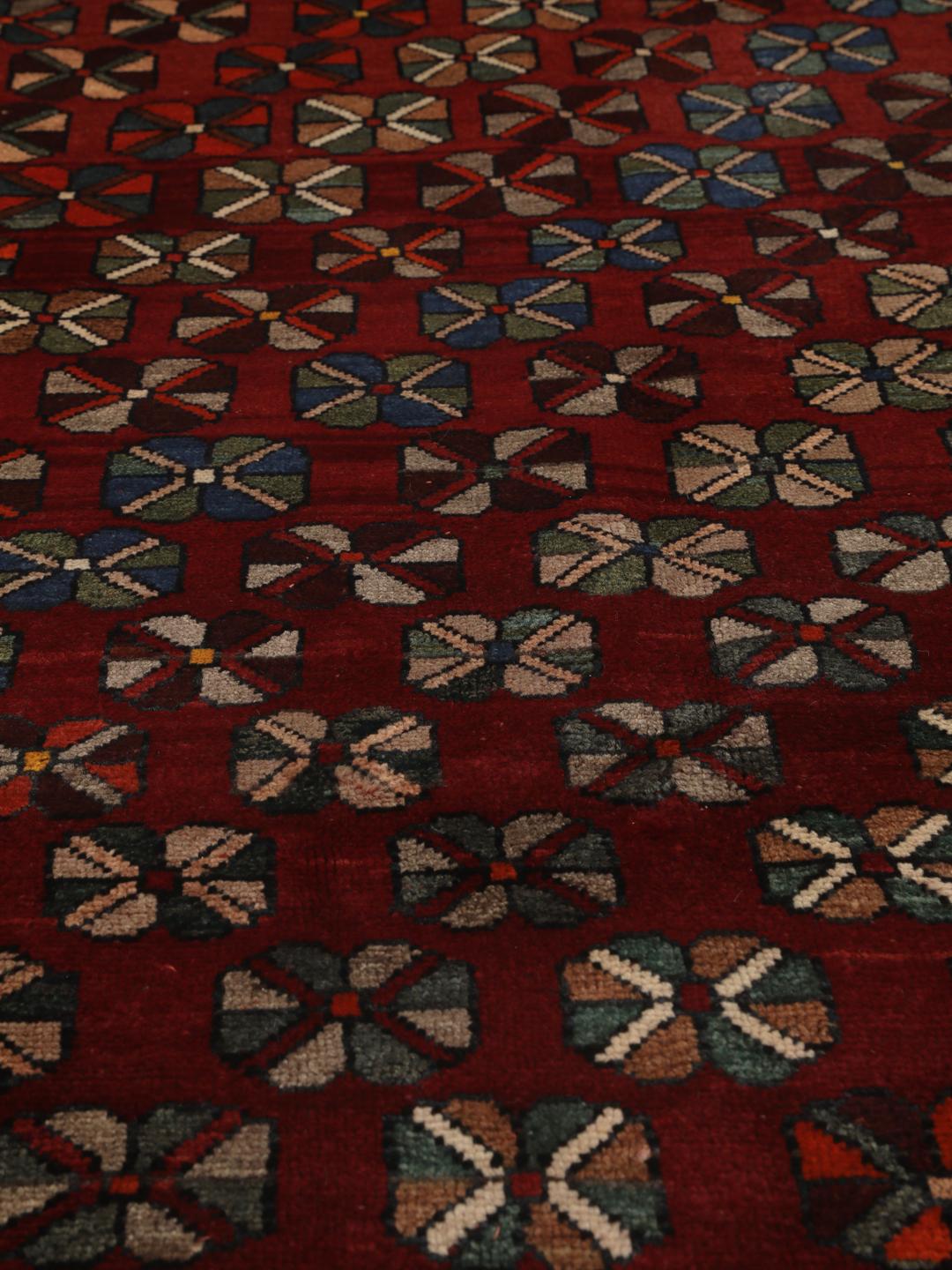 Et håndknyttet Ghashghai-tæppe fra Mellemøsten med en rig rød bundfarve og geometriske blomstermotiver.