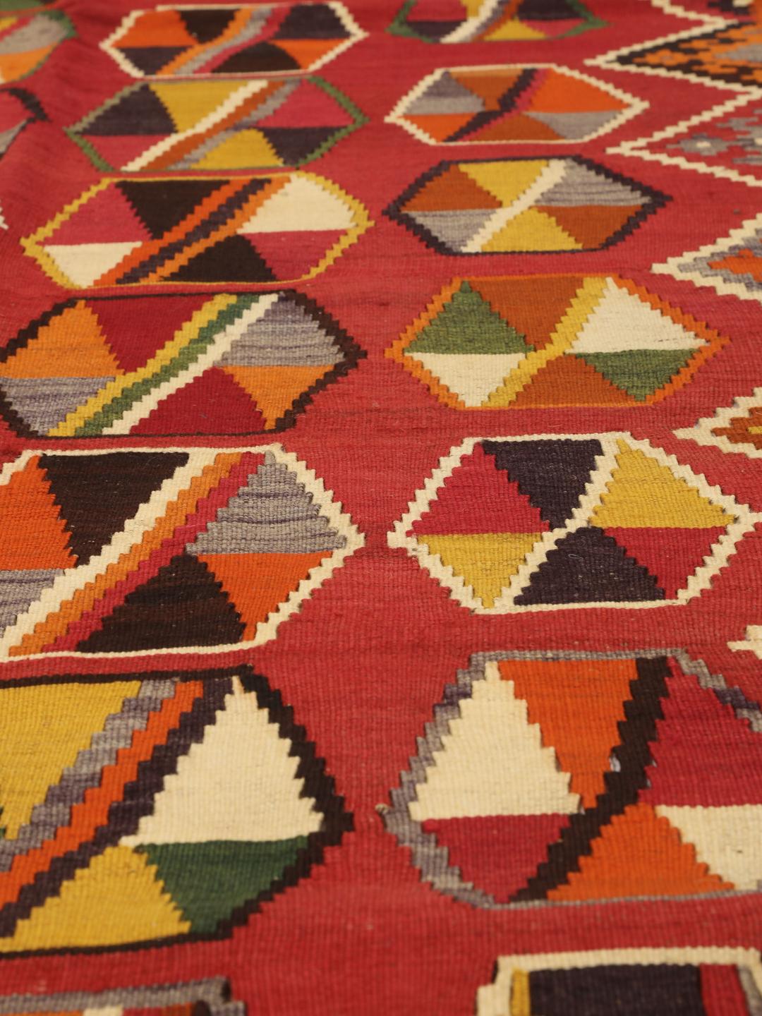 Et håndvævet vintage-kelimtæppe fra Mellemøsten med en rød flade og geometriske motiver.