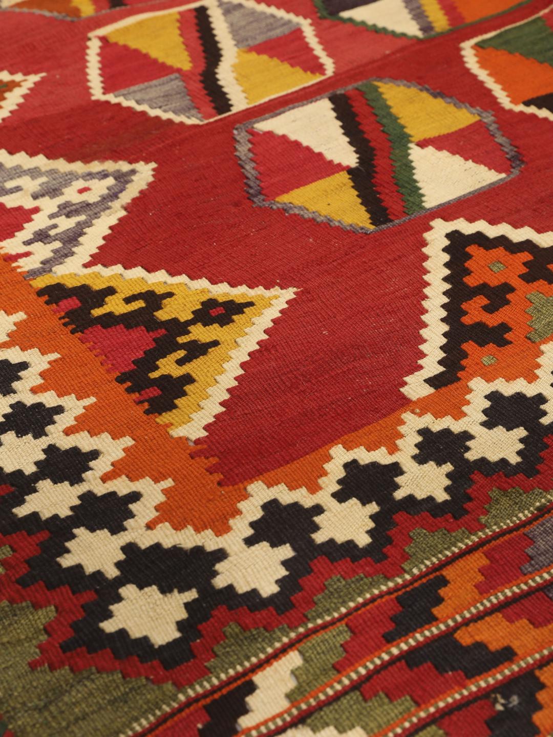Et håndvævet vintage-kelimtæppe fra Mellemøsten med en rød flade og geometriske motiver.