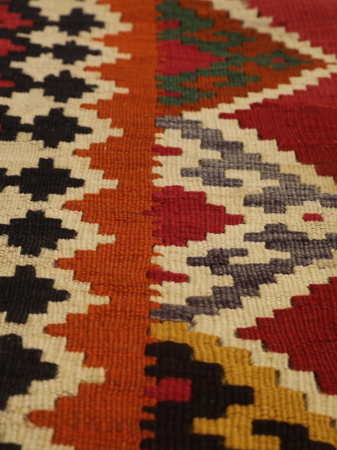 Et håndvævet vintage-kelimtæppe fra Mellemøsten med en rød flade og geometriske motiver.