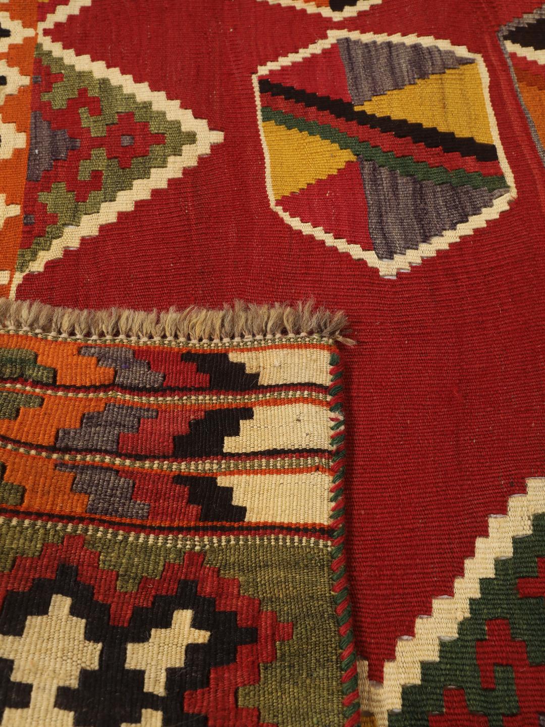 Et håndvævet vintage-kelimtæppe fra Mellemøsten med en rød flade og geometriske motiver.