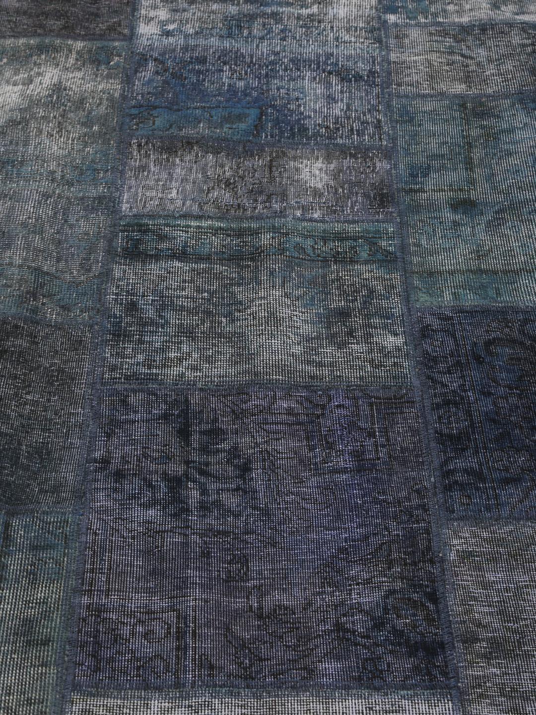 Een groot rechthoekig patchwork vloerkleed met diverse tinten donkerblauw en grijs, handgemaakt in het Midden-Oosten.