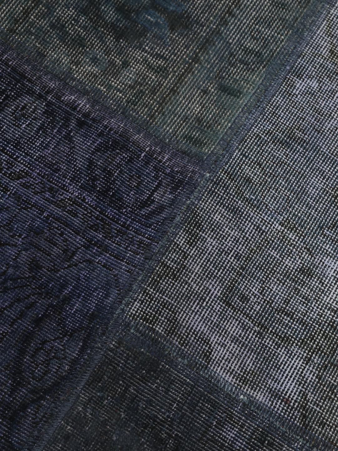 Een groot rechthoekig patchwork vloerkleed met diverse tinten donkerblauw en grijs, handgemaakt in het Midden-Oosten.
