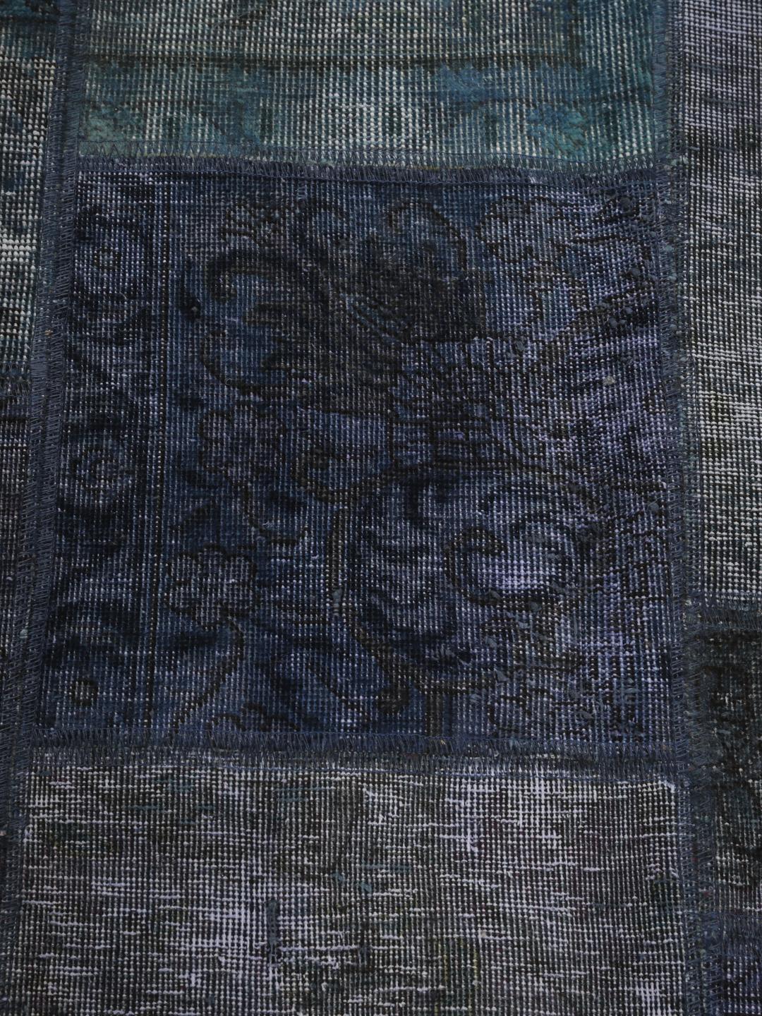 Een groot rechthoekig patchwork vloerkleed met diverse tinten donkerblauw en grijs, handgemaakt in het Midden-Oosten.